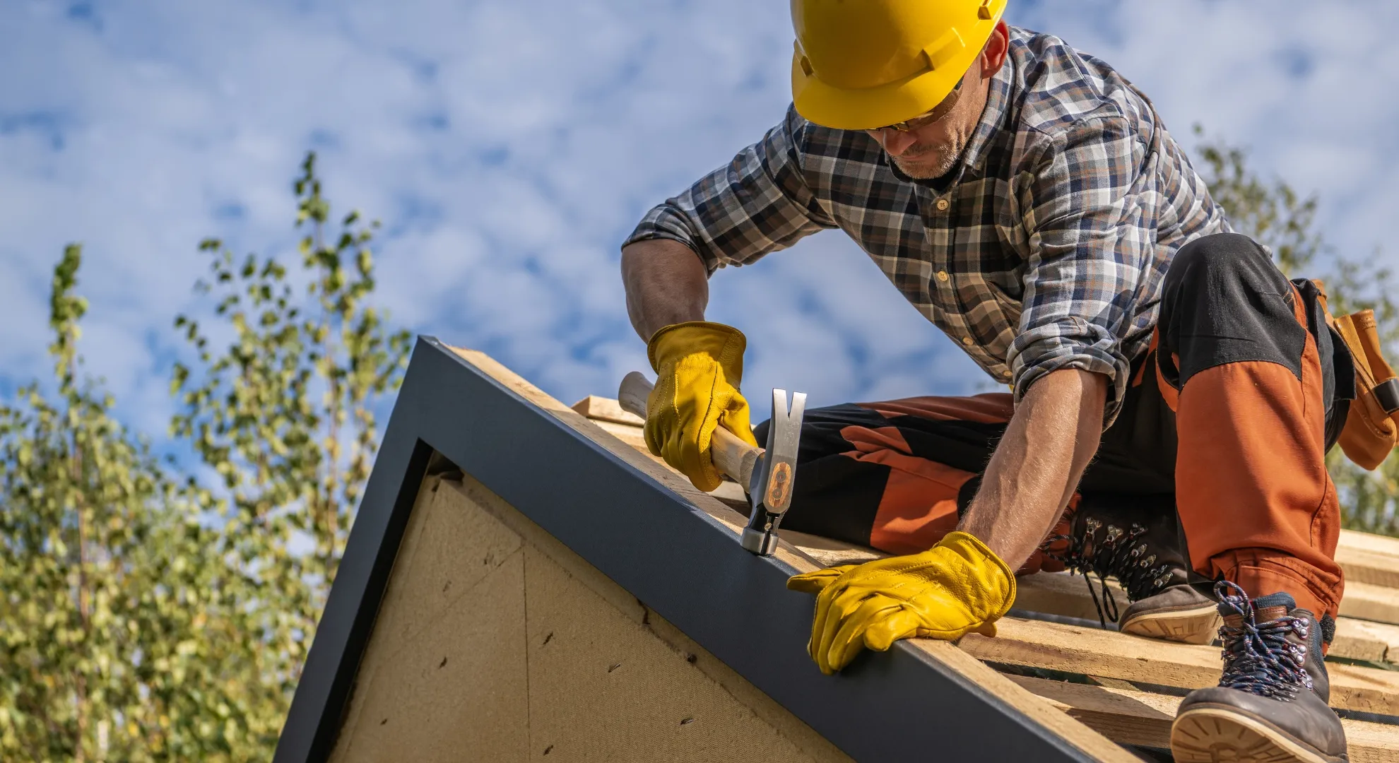 Professional roofer in yellow hard hat installing dark shingles